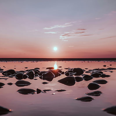 A pink and purple sunset over a wet sandy beach, meant to inspire hope and calm after trauma