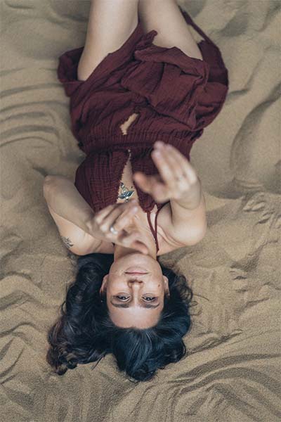 A woman laying on rumpled sheets, reaching for the camera as if seeking help for hypersexuality