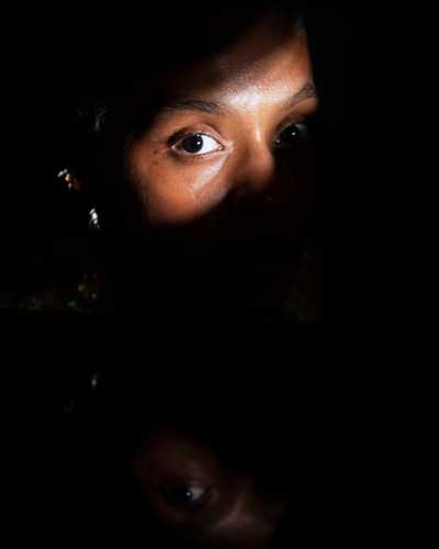 A Black woman shrouded in darkness with only a bar of light illuminating her eye
