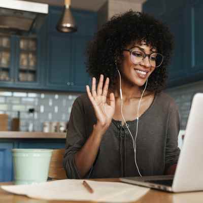 A Black woman waves hello toward her laptop while sitting in her kitchen for her remote CPT therapy session A Black woman waves hello toward her laptop while sitting in her kitchen for her remote CPT therapy session