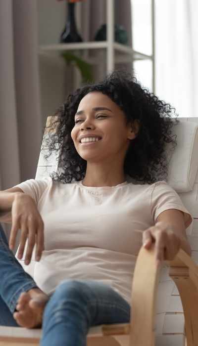 A woman sits casually in a chair, smiling and relaxed after undergoing CPT trauma-focused therapy