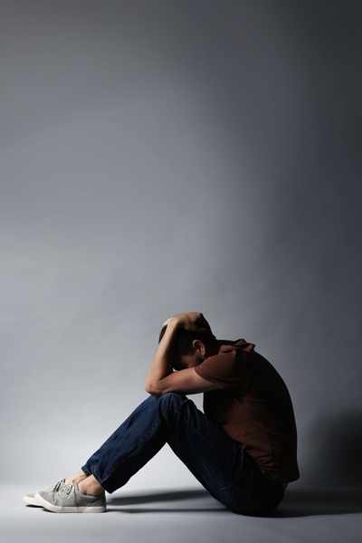 A woman sits on the floor in dim lighting, holding her head in her hands as she struggles with relational trauma