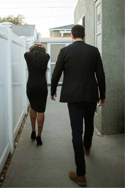 A woman walks ahead of a man with her hands covering her head as the man takes large steps to catch up to her during an argument
