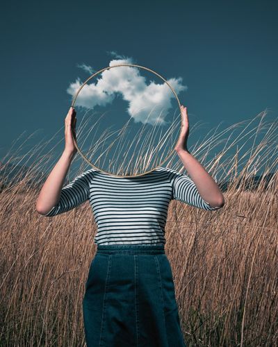 A woman holds a large round mirror in front of her head showing the sky and grass beyond to illustrate feeling disconnected from your body as in depersonalization derealization or dissociation