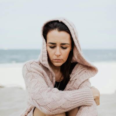 A woman sits with eyes downcast on the beach as she struggles with self-blame trying to make sense of her trauma