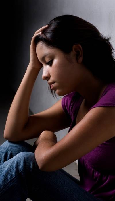 A woman sits with her back against a wall as she struggles with self-blame after trauma